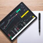 black ipad with stock market on screen on wooden table